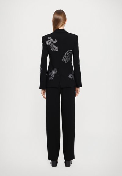 Černý oblek složený z přiléhavého saka s jemnými stříbrnými paisley výšivkami a odpovídajícími širokými kalhotami. Hladká textilie.