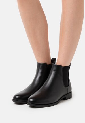 Botas de tobillo de cuero negro con paneles elásticos laterales, puntera redonda, tacón bajo apilado y superficie texturizada. Diseño minimalista, sin herrajes visibles.