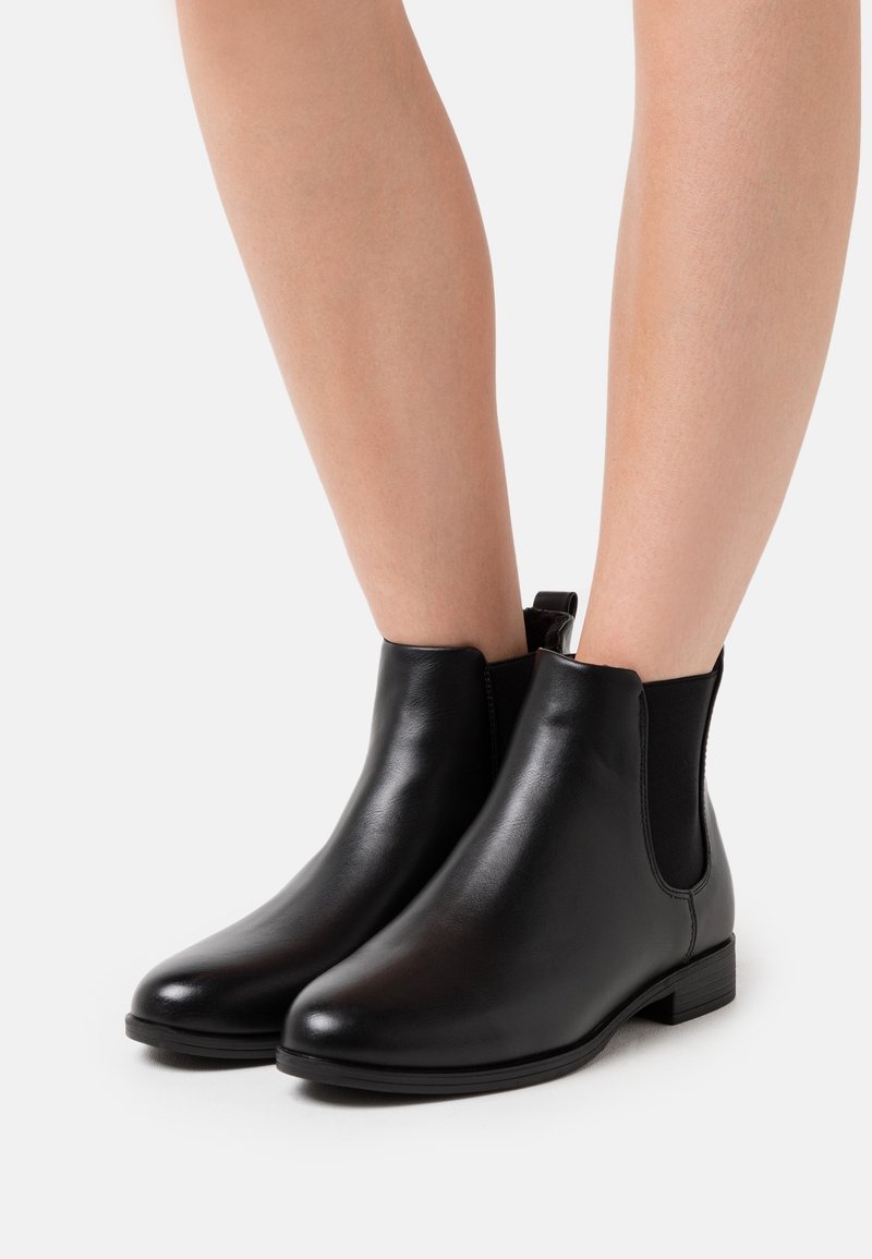 Botas de tobillo de cuero negro con paneles elásticos laterales, puntera redonda, tacón bajo apilado y superficie texturizada. Diseño minimalista, sin herrajes visibles.