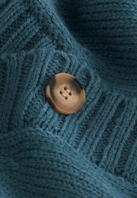Knit fabric in dark teal with a ribbed texture, featuring a light brown button with four holes positioned prominently on the material.