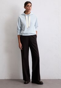 Helles blaues Hoodie mit weißem Kordelzug, kombiniert mit schwarzen weiten Hosen und dunklen Schuhen. Einfaches Design und weiche Texturen.