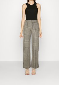 Black sleeveless top paired with high-waisted, wide-leg plaid trousers in gray and beige, featuring a checkered pattern. Strappy heeled sandals.
