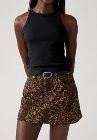 Zwart geribbeld tanktop gecombineerd met een bruine denimrok met luipaardprint. De rok heeft zakken en een riem met een zilveren gesp.