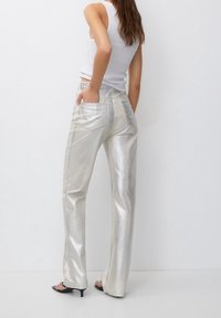 Srebrne, metaliczne spodnie o szerokich nogawkach z g�ładką teksturą. Posiadają dwie tylne kieszenie i wysoką talię. Noszone z dopasowanym białym topem na ramiączkach.