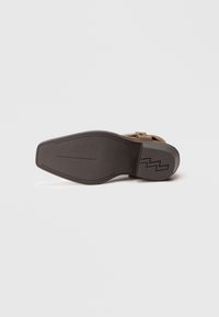 Zapato de cuero marrón con suela plana, que presenta un diseño elegante, costuras sutiles y un patrón en zigzag en la parte inferior para mayor tracción.