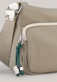 Beige nylon crossbody bag with silver hardware, featuring a front zip pocket and green cord detail with a metal accent.