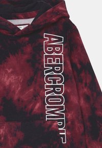 Sweatshirt à capuche tie-dye en bordeaux et noir, avec une poche avant et "ABERCROMBIE" imprimé verticalement en blanc.