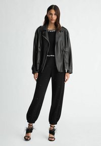 Giacca di pelle nera sopra una maglietta nera e pantaloni neri con embellishments. Le calzature presentano fasce nere e accenti di piume, con una vestibilità rilassata.