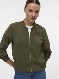 Veste bomber vert olive en tissu lisse, fermeture éclair, poignets en bord-côte et deux poches latérales. Associée à un jean pour un style décontracté.