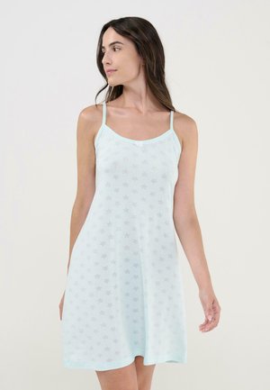 Mujer con vestido azul claro sin mangas, con tirantes finos y pequeños estampados de estrellas, mirando hacia su izquierda contra un fondo liso.