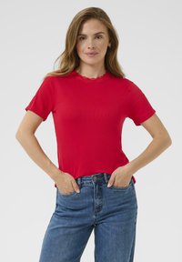 T-shirt rouge à manches courtes avec un col rond orné de dentelle, associé à un jeans bleu taille haute, mettant en valeur une silhouette ajustée.