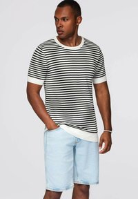 Suéter de punto a rayas en blanco y negro, de manga corta y cuello redondo, combinado con pantalones cortos de mezclilla azul claro, con un corte relajado.