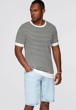 Zwart-witte gestreepte gebreide trui met korte mouwen en een ronde hals, gecombineerd met lichtblauwe denimshorts met een relaxte pasvorm.