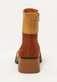 Botín de cuero marrón y beige con tacón grueso, texturas contrastantes y detalles de costura, que cuenta con una cremallera lateral para facilitar su uso.