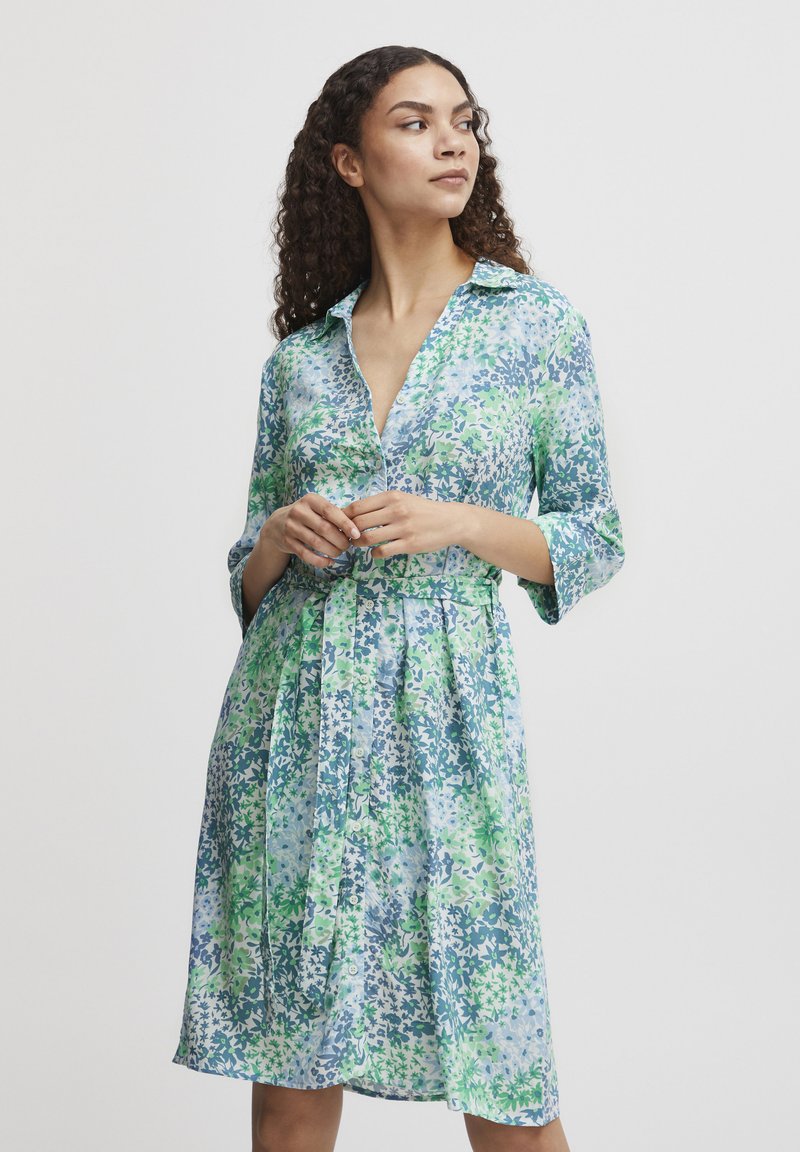 Rochie florală în nuanțe de albastru și verde, cu un guler, închidere prin nasturi și talie legată. Fabricată dintr-un material ușor, cu un design fluid.