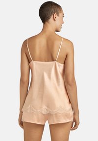 Camisole en satin pêche avec des bretelles réglables, ornée d'une délicate dentelle le long de l'ourlet, texture douce et coupe relaxée.