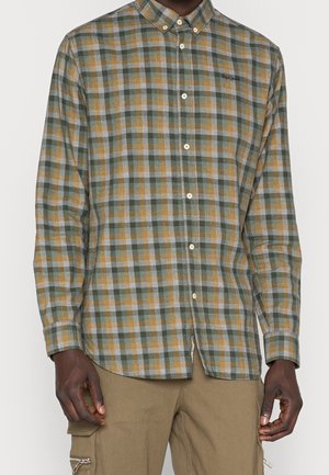 Camisa de manga larga con botones y patrón de cuadros en verde, gris y amarillo, usada con pantalones cargo beige.