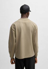 Beige Langarmhemd mit lockerer Passform, rundem Halsausschnitt und weichem Material. Verfügt über einen geraden Saum und ein lässiges Design.