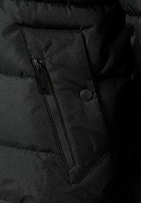 Crna podstavljena jakna s patentnim zatvaračem na prednjem džepu, teksturirana tkanina i kružni logo na džepu. Mekana, glatka završna obrada.