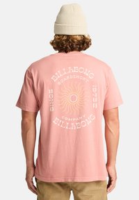 Pink cotton t-shirt featuring a sun graphic and "Billabong" text on the back. Relaxed fit, short sleeves, loop neck, soft texture.