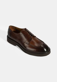 Bruine leren dresschoen met een ronde neus, subtiele stikdetails en een gestructureerde buitenzool. Voorzien van veters en een gladde afwerking.