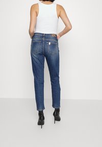 Jeans de denim azul ajustados con bolsillos traseros, un ligero desvanecimiento y una cintura de altura media; combinados con botas de tacón alto negras.