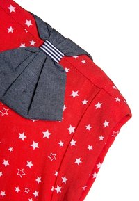 Roter Stoff mit weißen Sternen und einer dunkelblauen Schleife, die mit einem weiß-blau gestreiften Band im Schulterbereich eines Kleidungsstücks gebunden ist.