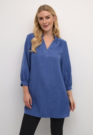 Tunic blu, a maniche lunghe, con scollo a V, dettagli arricciati sulle spalle e vestibilità comoda, abbinata a pantaloni neri. Tessuto liscio.