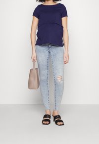 Mörkblå kortärmad topp med lagerdesign, ihop med ljusblå skinny jeans med knäskår, svarta klacksandaler och en beige tote.