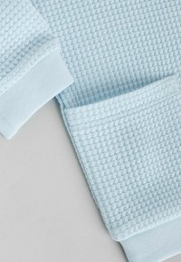 Lichtblauwe gebreide stof met een textuur in wafelpatroon. Mouwen in een gladder blauw materiaal. Comfortabel en casual ontwerp.