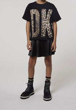 Enfant portant un t-shirt noir avec de grandes lettres imprimées léopard "DK", une jupe noire, des chaussettes imprimées léopard et des bottes noires à lacets.