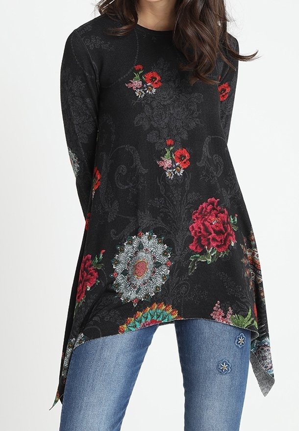 Tunique noire à manches longues ornée de motifs floraux rouges et bleus. L'ourlet est asymétrique. Portée avec un jean bleu décoré d'accents floraux.