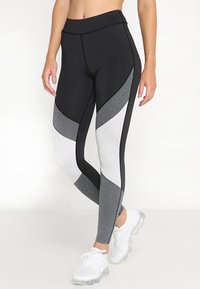 Leggings atletici a vita alta con una combinazione di pannelli neri, bianchi e grigi. Realizzati in un tessuto elastico e traspirante con una texture liscia.