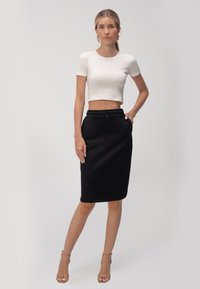 Biely skrátený tričko kombinované s čiernou sukňou po kolená, ktorá má elastický pás a šnúrku na stiahnutie. Modelka má na sebe béžové sandále na opätku.