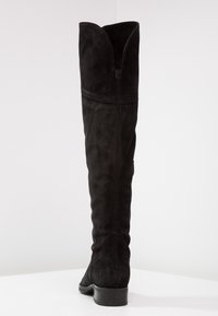 Botas negras encima de la rodilla en suave gamuza, con un puño ancho, detalles de costura y un tacón bajo apilado. Textura suave con un acabado mate.