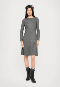 Abito grigio a maglia con maniche lunghe e una linea dritta, caratterizzato da una texture sottile. Indossato con stivali neri fino al ginocchio e un cerchietto multicolore.