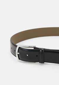 Ceinture en cuir noir au fini lisse, avec une boucle rectangulaire argentée et un dos en cuir brun contrastant. Comprend des trous pour l'ajustement.