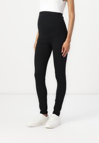 Zwarte zwangerschap leggings met een hoge elastische tailleband, zachte stof en aansluitend design, gecombineerd met witte sneakers.