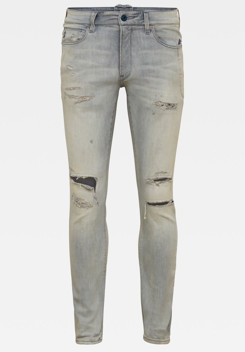 Jeans ajustados en denim azul claro deslavado, con detalles desgastados y roturas en las rodillas, diseño clásico de cinco bolsillos y cierre de botón azul.