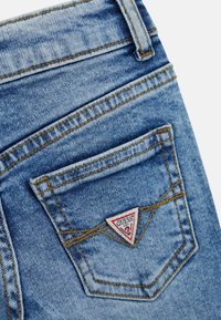 Ljusblå denimjeans med en blekt textur. Har en triangulär röd och vit logopatch på bakfickan med kontrasterande sömmar.