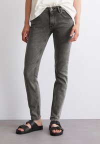 Šedé džíny z denimu se slim fit, pěti kapsami, zapínáním na knoflík a jemným vyblednutím, doplněné černými plochými sandály.