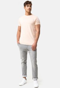 Helles rosa T-Shirt mit kurzen Ärmeln und rundem Ausschnitt, aus weichem Stoff; kombiniert mit hellgrauen Jeans mit umgeschlagenen Bündchen und weißen Sneakers.