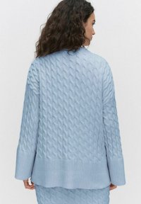 Ljusblå kabelstickad cardigan med ribbade ärmslut och nederkant, med ett texturerat mönster och avslappnad silhuett, sedd bakifrån.