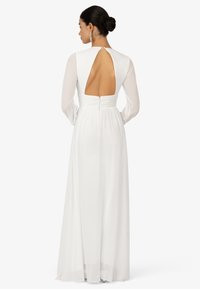 Robe longue blanche avec des manches longues, décolleté dans le dos, taille froncée et jupe lisse et fluide. Design minimaliste avec fermeture à boutons.
