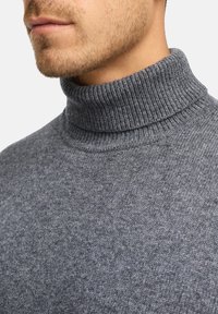 Pull en col roulé gris avec une texture côtelée et un col haut, fabriqué en tissu tricoté, présenté en gros plan autour du cou et du menton.