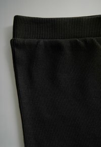 Schwarzer gerippter Stoff mit einer strukturierten Oberfläche. Verfügt über einen breiten, elastischen Bund, der für Komfort und Flexibilität in der Passform sorgt.