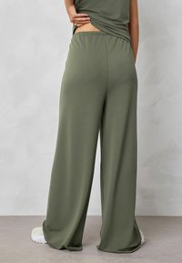 Olivegrüne, weit geschnittene Hosen mit weichem Stoff und elastischem Bund. Die Rückseite zeigt ein drapiertes Design für zusätzlichen Stil.