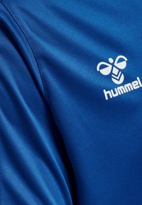 Blauer Sportstoff mit sichtbarer Naht und weißem hummel-Logo mit stilisierter Hummel und Text auf der rechten Seite.