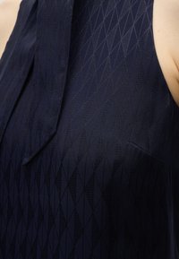 Μπλε ναυτικό αμάνικο ένδυμα με διακριτικό γεωμετρικό διαμαντένιο σχέδιο και υφασμάτινη ρευστή λεπτομέρεια κοντά στο ντεκολτέ.