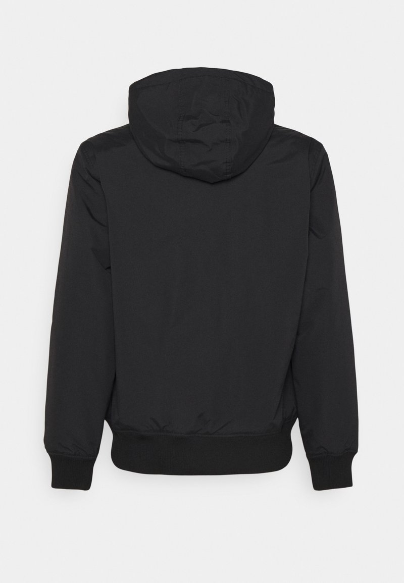 Giacca nera con cappuccio, dotata di polsini e vita elasticizzati, realizzata in un materiale liscio e resistente all'acqua, priva di loghi o motivi visibili.